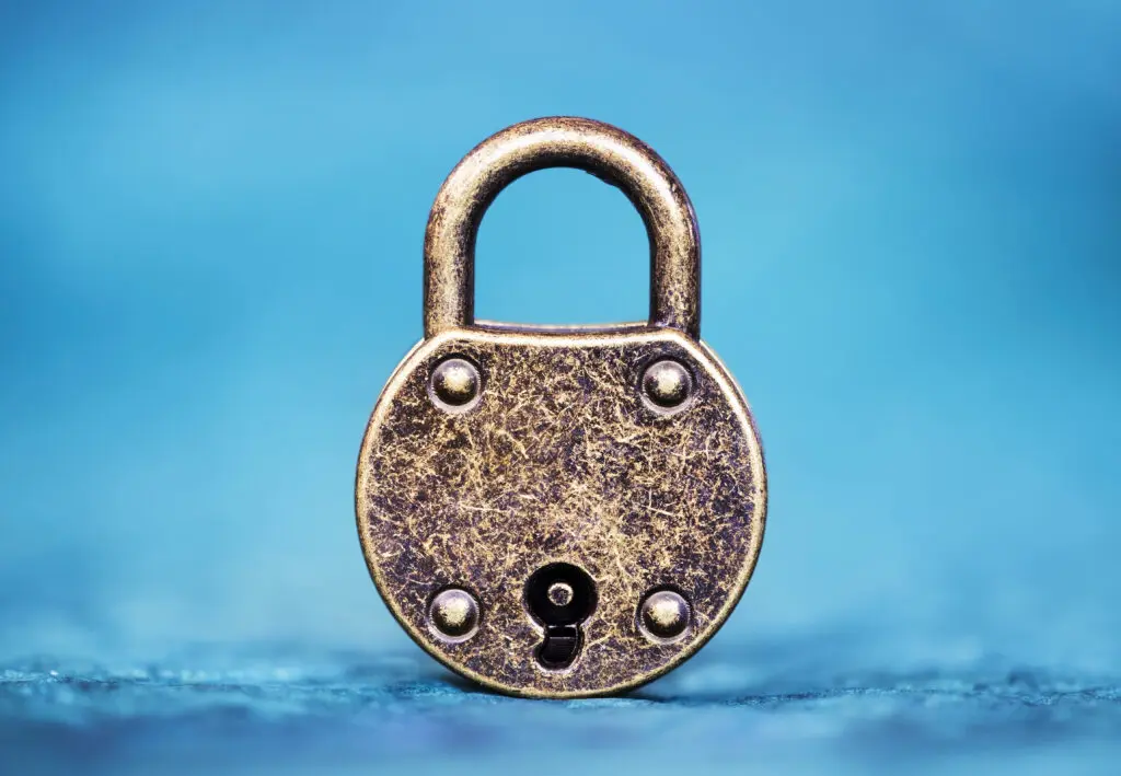 A close-up image of a vintage brass padlock positioned against a soft blue background. The padlock has a round shape with a keyhole and is slightly tarnished, showing signs of wear.
