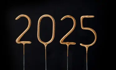 The image shows the numbers "2025" in a stylized, golden font on thin metal stakes, set against a black background.