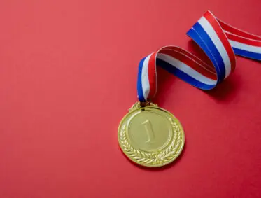 A gold medal with the number "1" engraved on it hangs from a red, white, and blue striped ribbon. The background is a solid red color.