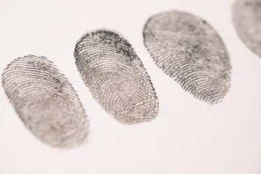 A close-up image of several inked fingerprints arranged in a row on a light background. The fingerprints display distinct patterns and ridges, showcasing the unique characteristics of each print.